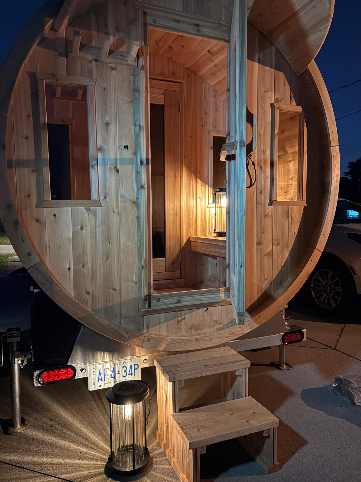 Nord Steam cedar barrel sauna at dusk — enclosed anteroom open, warm interior lighting glowing